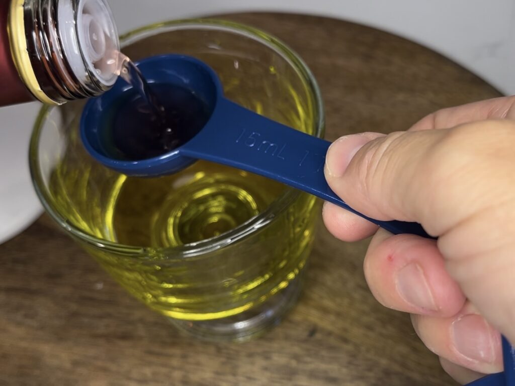 Adding vinegar to olive oil into a glass bowl on the counter