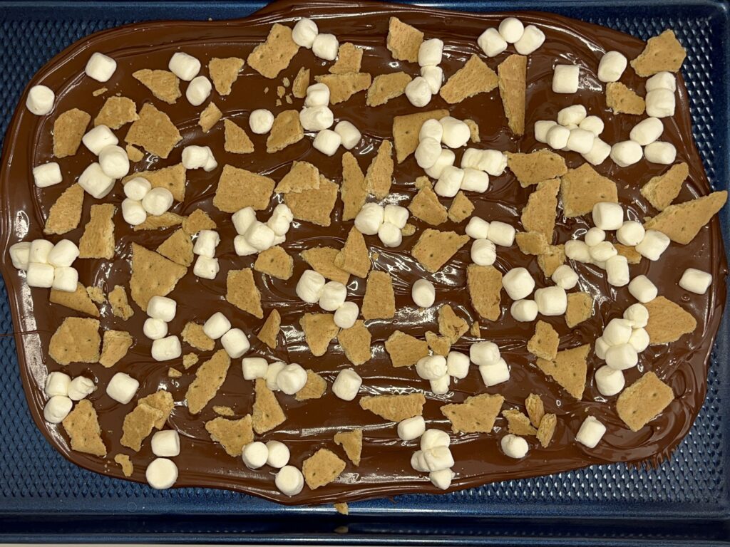 Melted chocolate on a baking sheet with mini marshmallows and graham crackers on it on a baking sheet