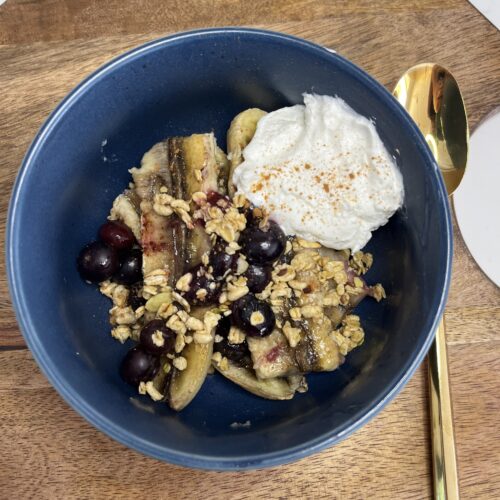 Banana, blueberries, cinnamon, maple syrup, palin yogurt and granola in a bowl.