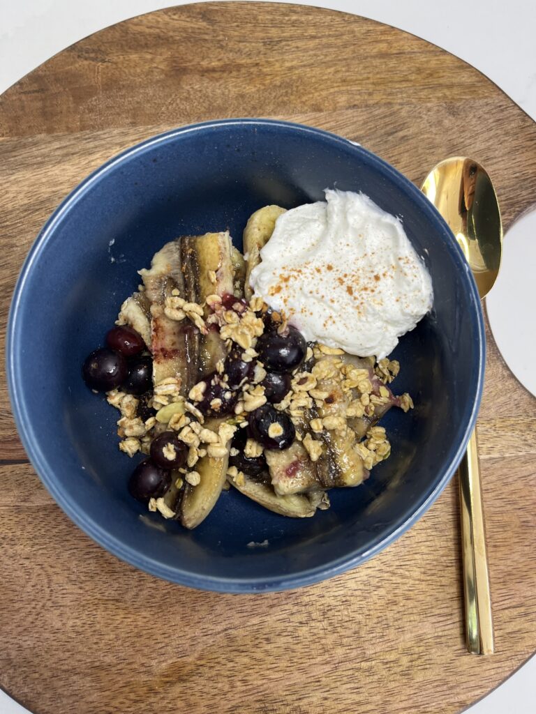 Banana, blueberries, cinnamon, maple syrup, palin yogurt and granola in a bowl.