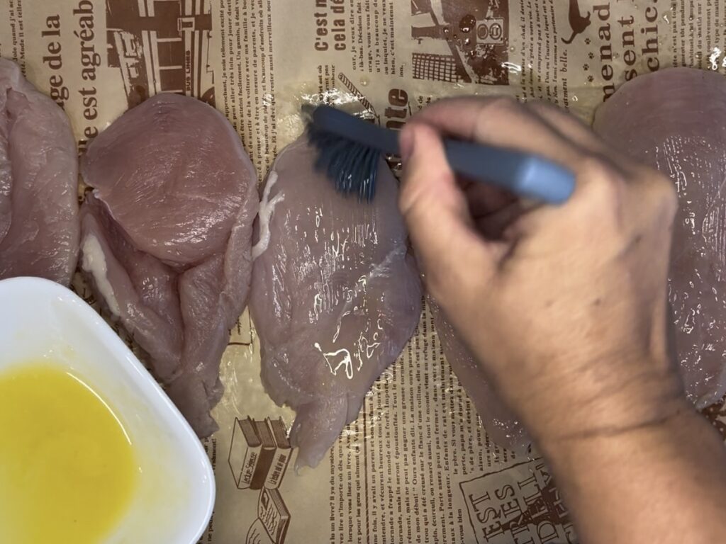 Brushing chicken breasts with butter on parchment paper on a baking sheet