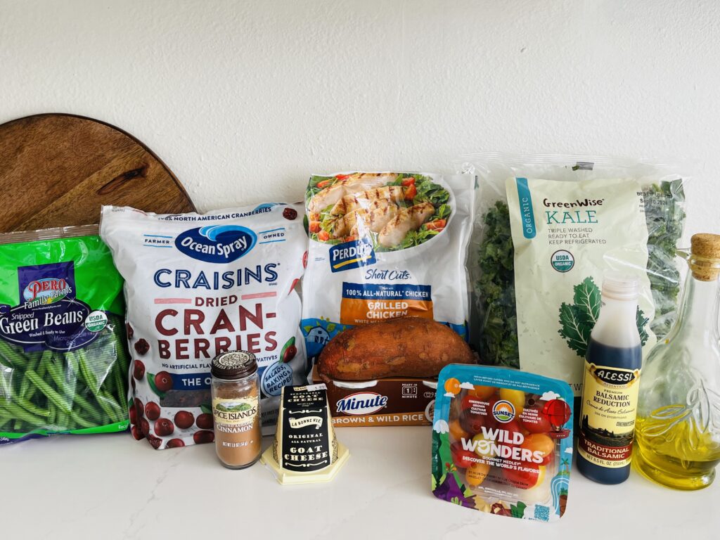 Harvest bowl ingredients- pre-packaged grilled chicken breasts, kale olive oil, cherry tomatoes, balsamic glaze, goat cheese, minute rice, sweet potato, green beans on the counter 
