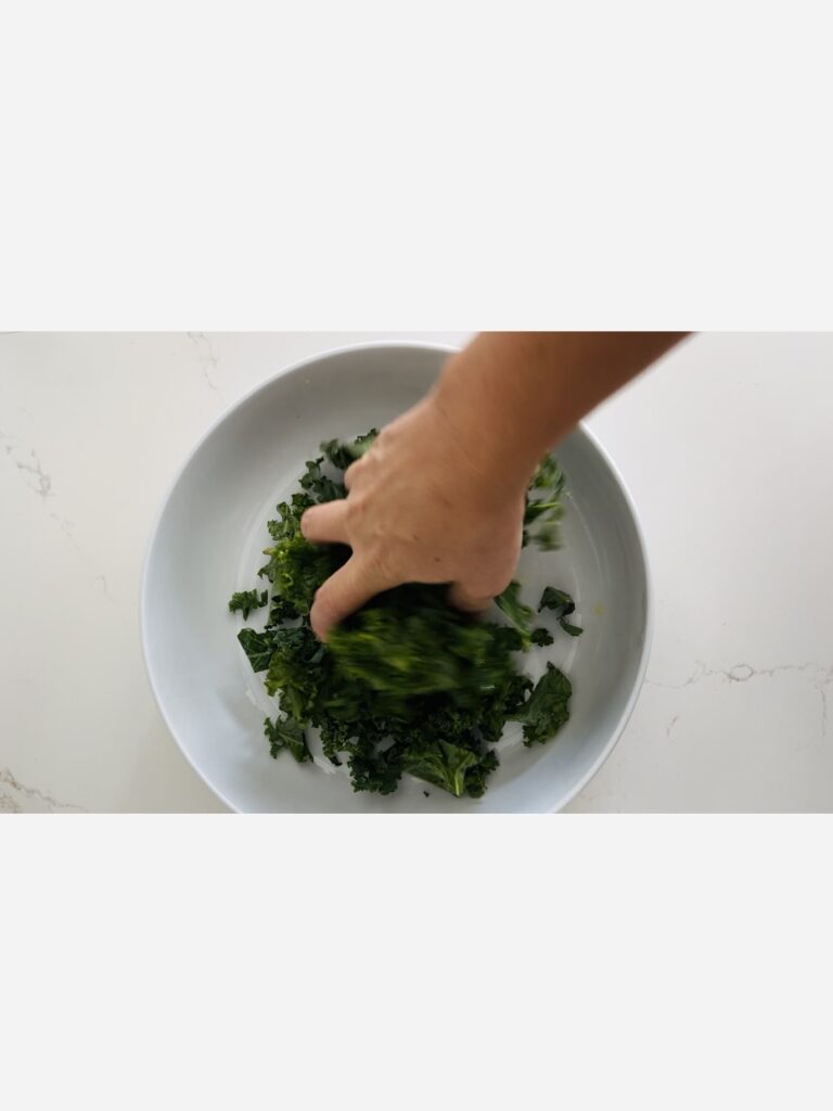 Massaging olive oil into the kale with hands in a wide bowl