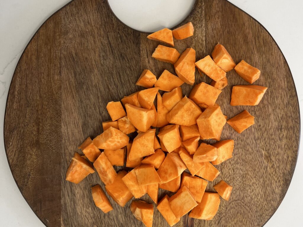 A sweet potato cut up into bite size pieces on a cutting board