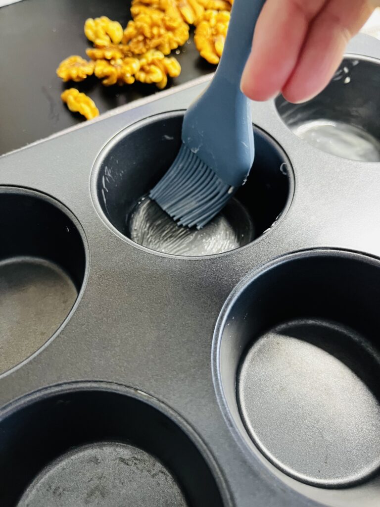 Using a basting brush, and applying melted butter to each muffin tin.