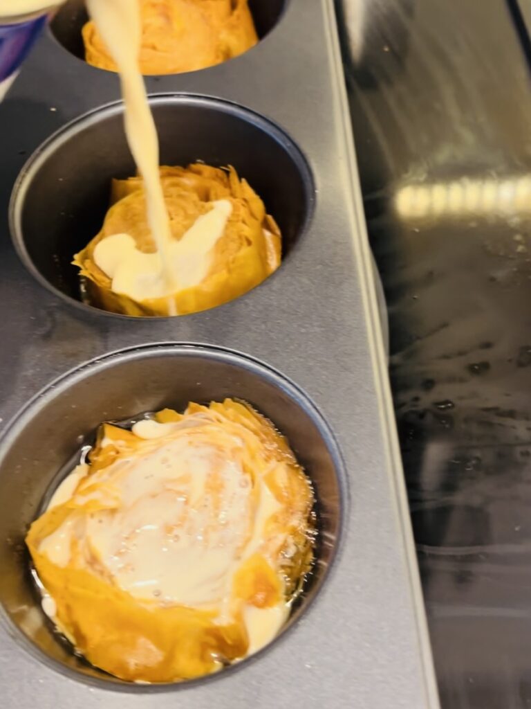 Pouring evaporated milk onto phyllo pieces in muffin tins