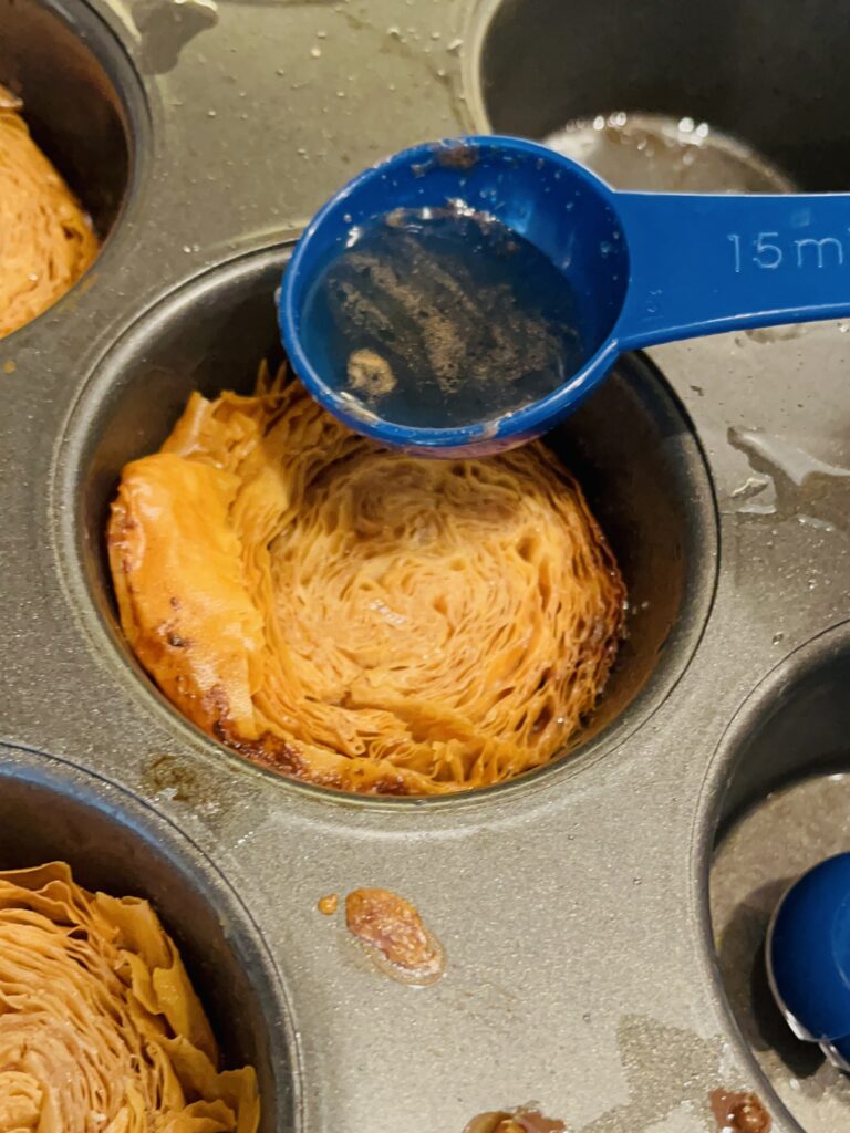 Pouring 1 Tablespoon of syrup over the phyllo pieces in a muffin tin