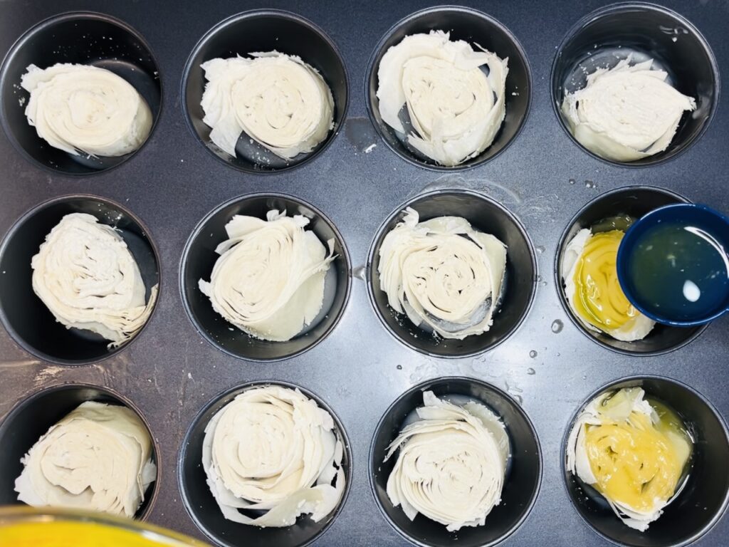 Pouring melted butter over phyllo pieces while in muffin tin.