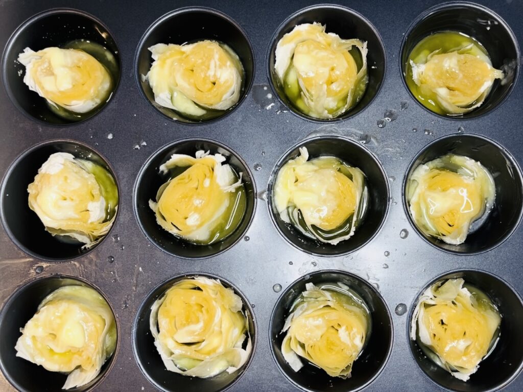 Melted butter over phyllo pieces in muffin tin