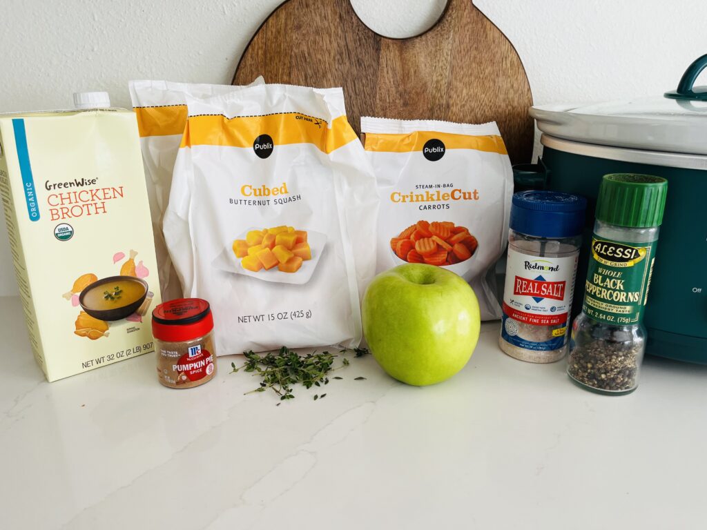 Chicken broth, 2 bags of frozen cubed butternut squash, 1 bag of frozen carrots, green apple pumpkin pie spice, salt and pepper, and sprigs of thyme on the counter.