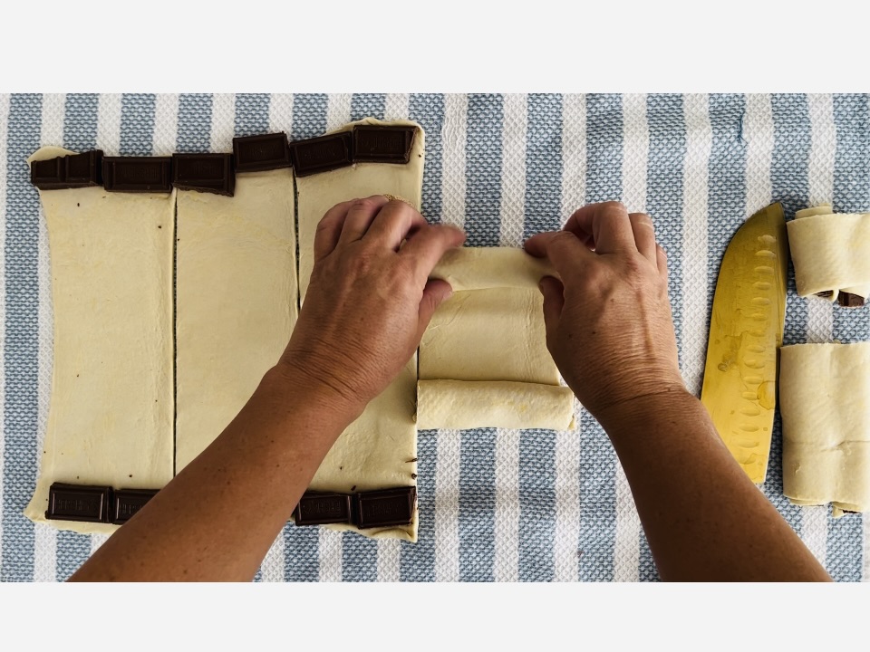 Rolling puffed pastry and chocolate together from opposite edges on a kitchen towel