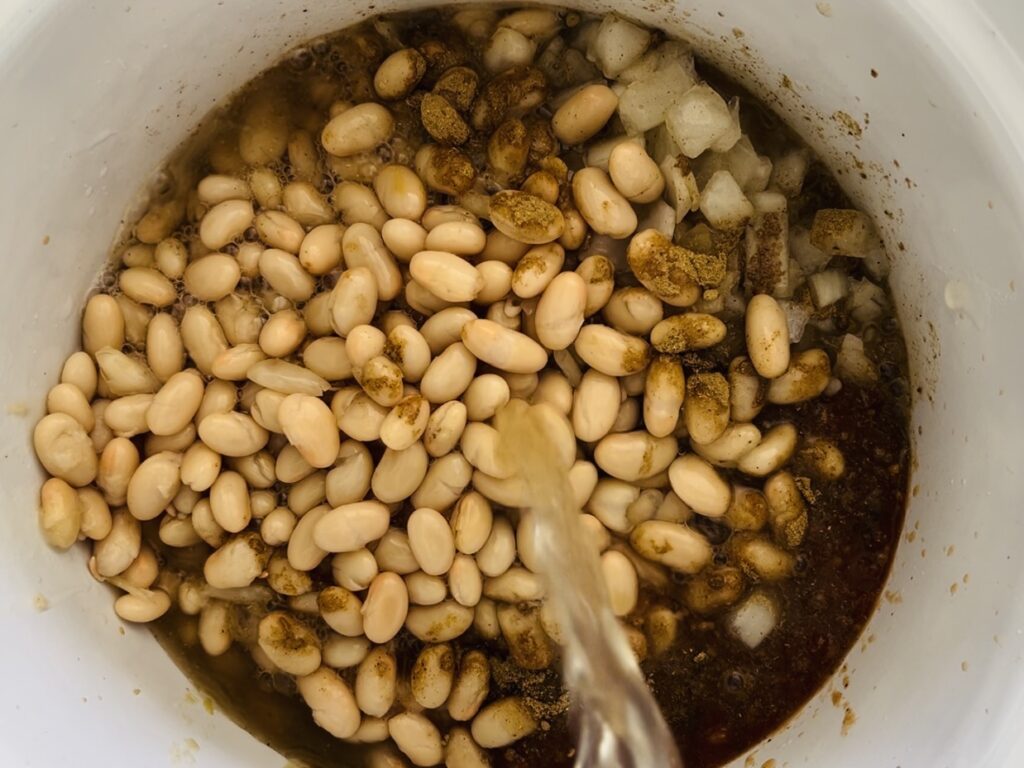 Pouring chicken broth over beans in the slow cooker.