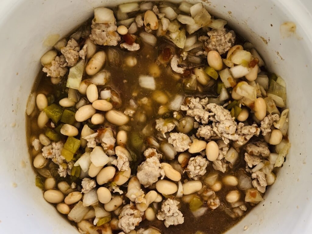 Browned chicken, onions, green chilies, beans, cumin and broth and mixed together in the slow cooker.