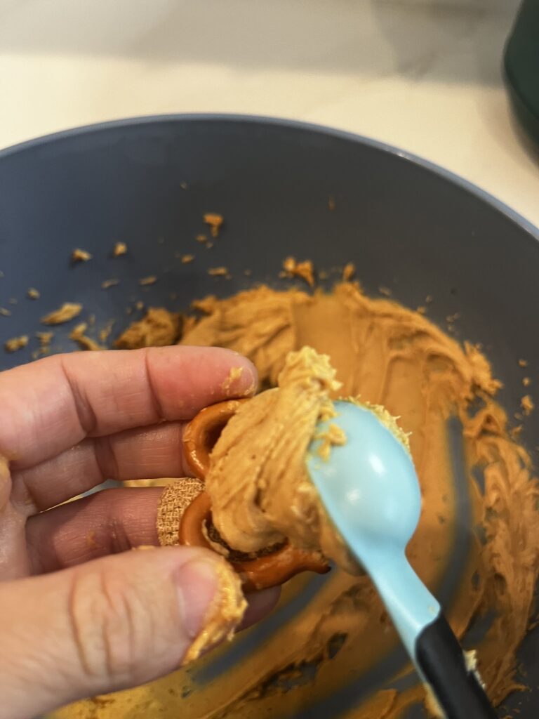 Smearing nut butter mixture onto a pretzel using a small measuring spoon.