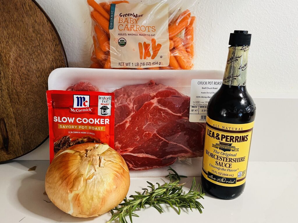 Carrots, chuck pot roast, Worcestershire sauce, rosemary sprigs, slow cooker herb and spice packet and an onion on the counter