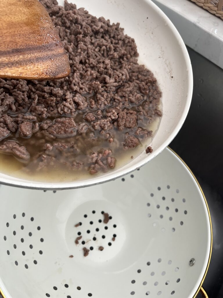 Draining excess fat and water from browned beef into a strainer