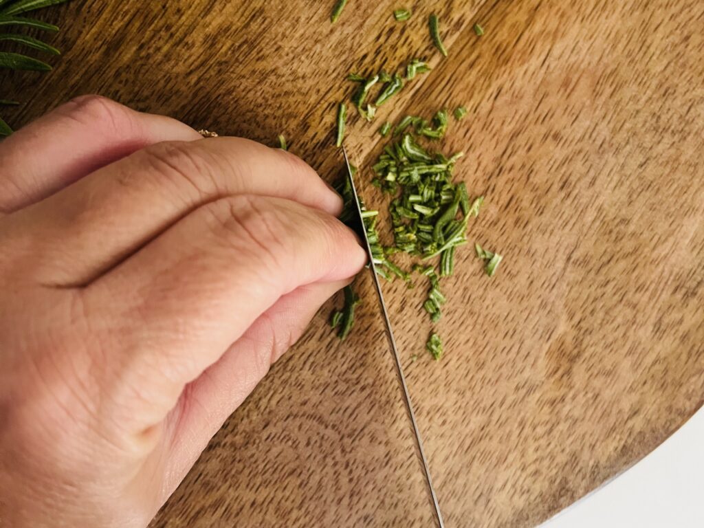 Using a knife to mince rosemary.