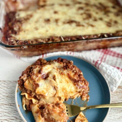 a slice of lasagna on a plate with a fork next to a casserole dish of lasagna