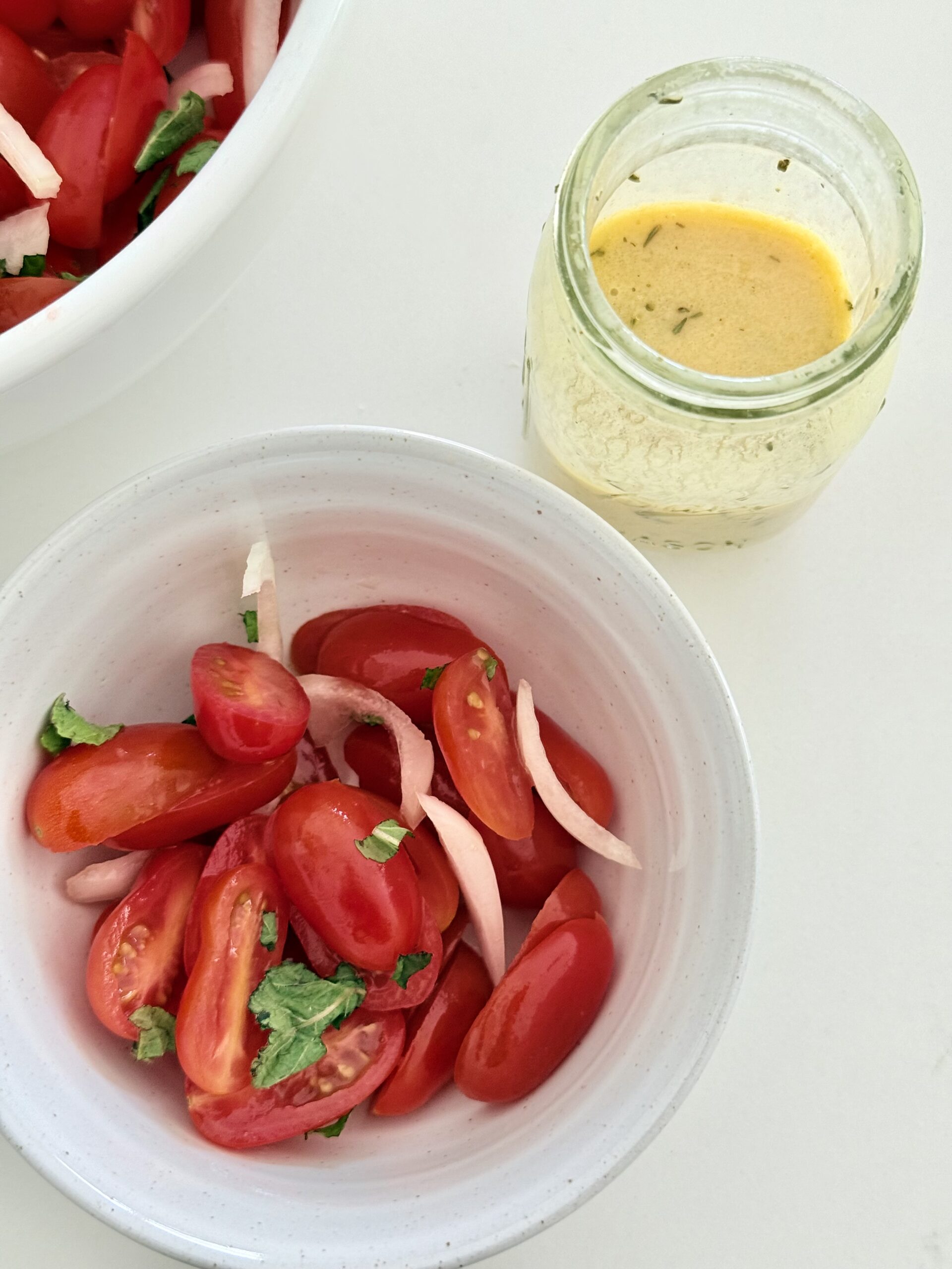 French Bistro Vinaigrette in a small glass jar on the counter beside a bowl with tomato and onion salad on the counter.