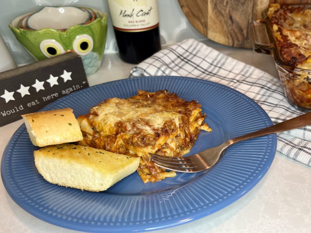 lasagna on a plate next to garlic bread