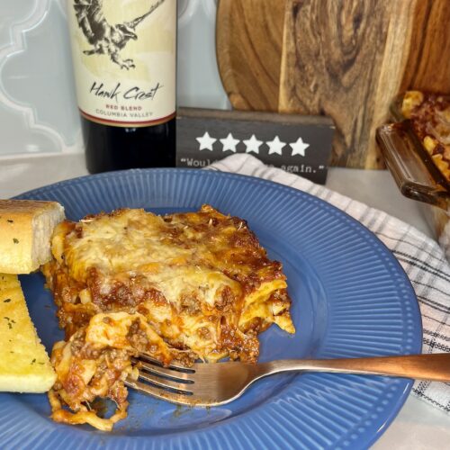 Cooked lasagna on a blue plate with garlic bread