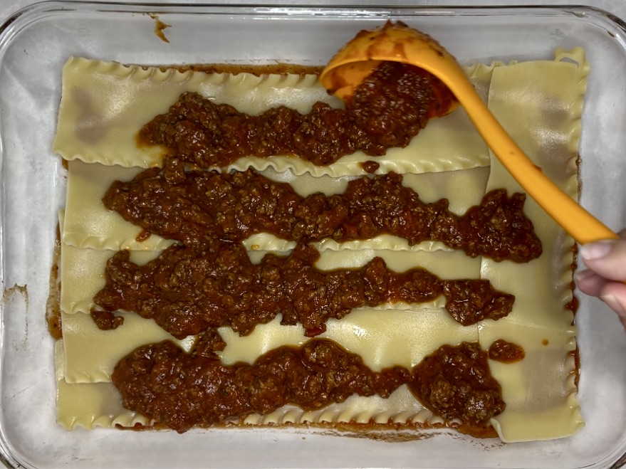 sauce being spread over lasagna noodles in a dish