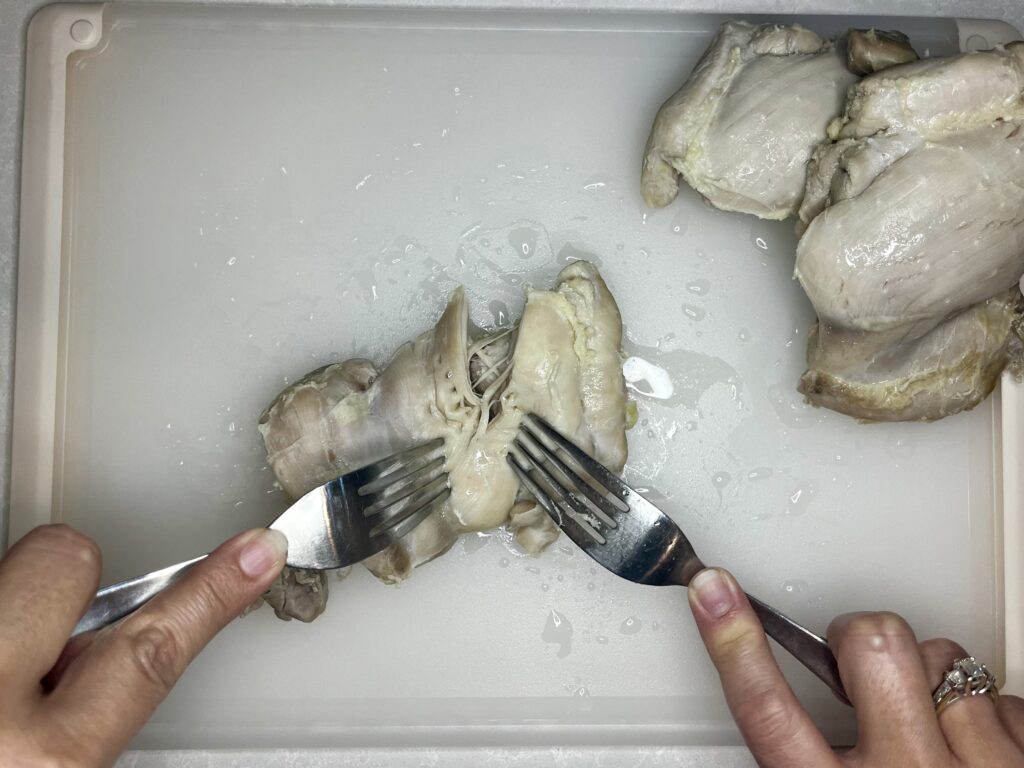 cooked chicken being shredded by 2 forks