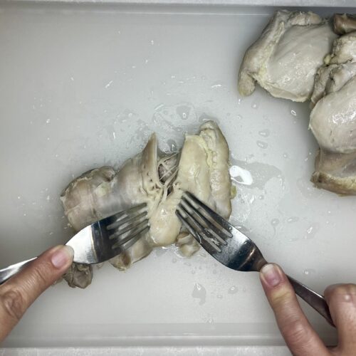 cooked chicken being shredded by 2 forks