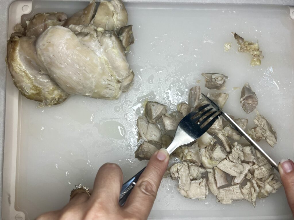 cooked chicken being cut up into cubes