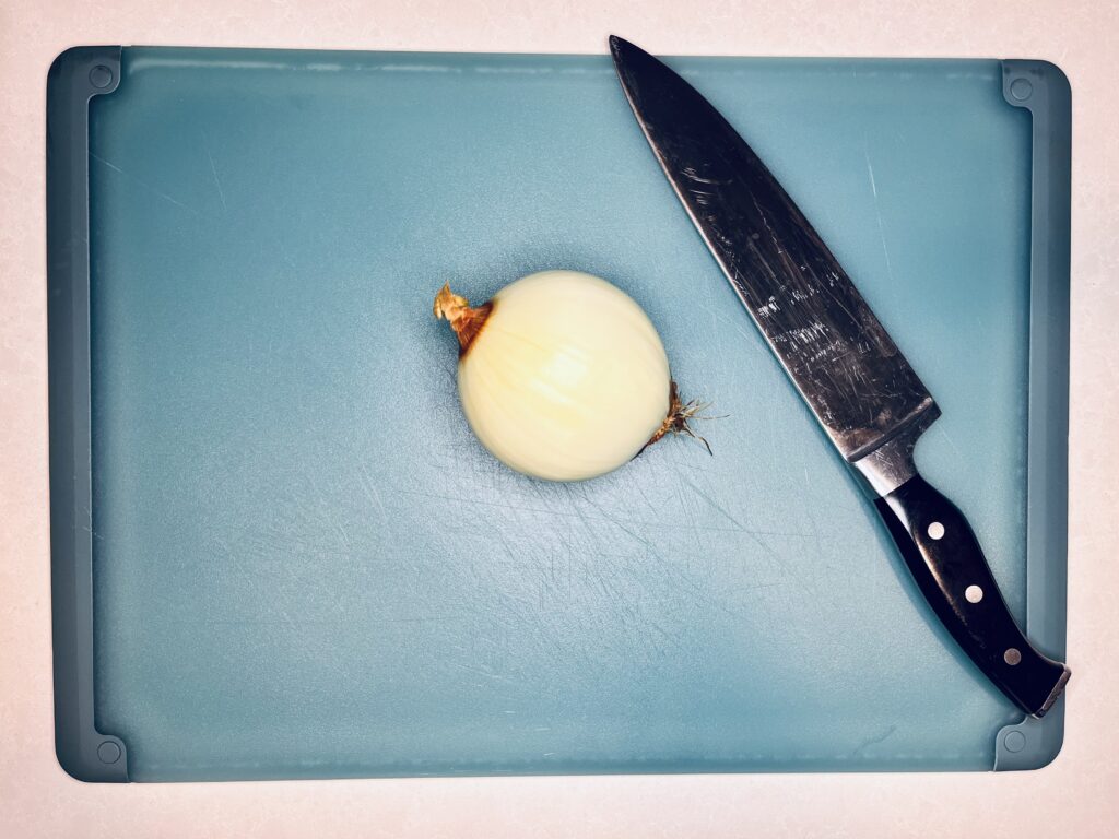 a whole onion on a cutting board next to a kitchen knife