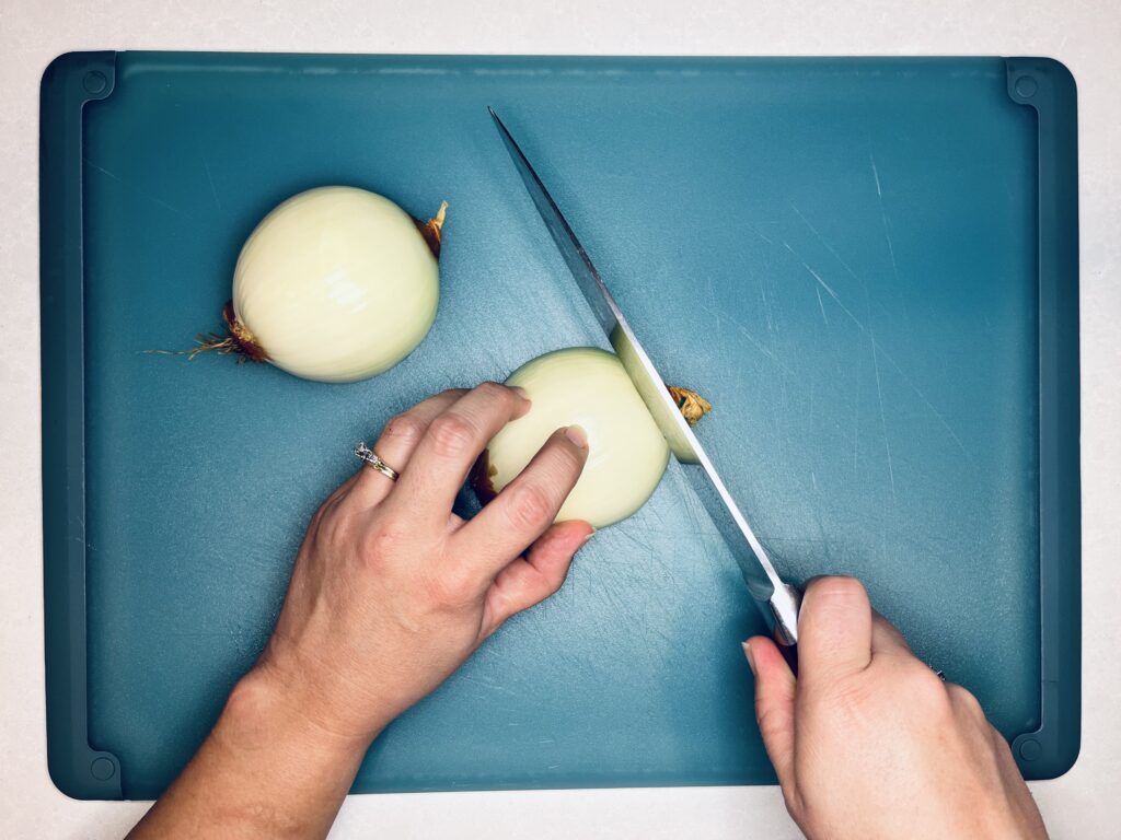 A knife slicing the top off of the onion