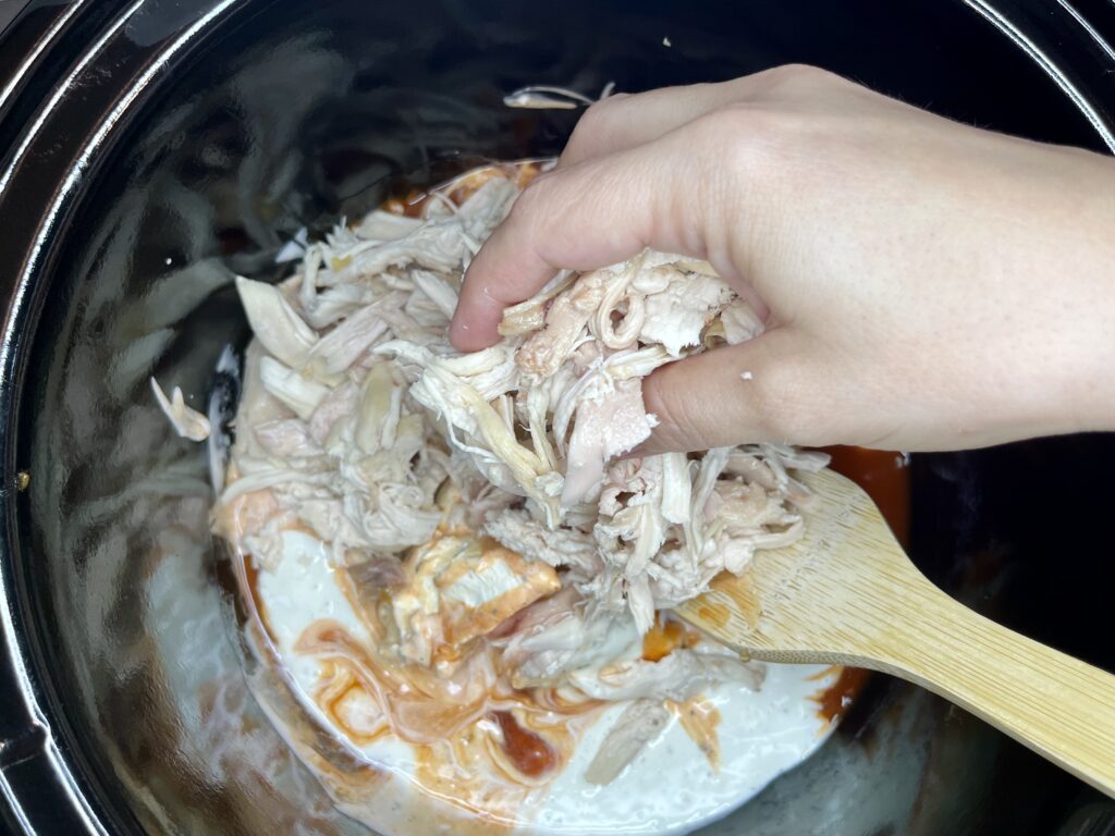 shredded chicken being added to a slow cooker