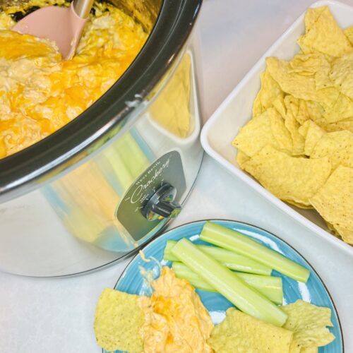 hot dip in a slow cooker next to a plate and a bowl of chips