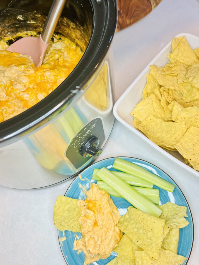 hot dip in a slow cooker next to a plate and a bowl of chips