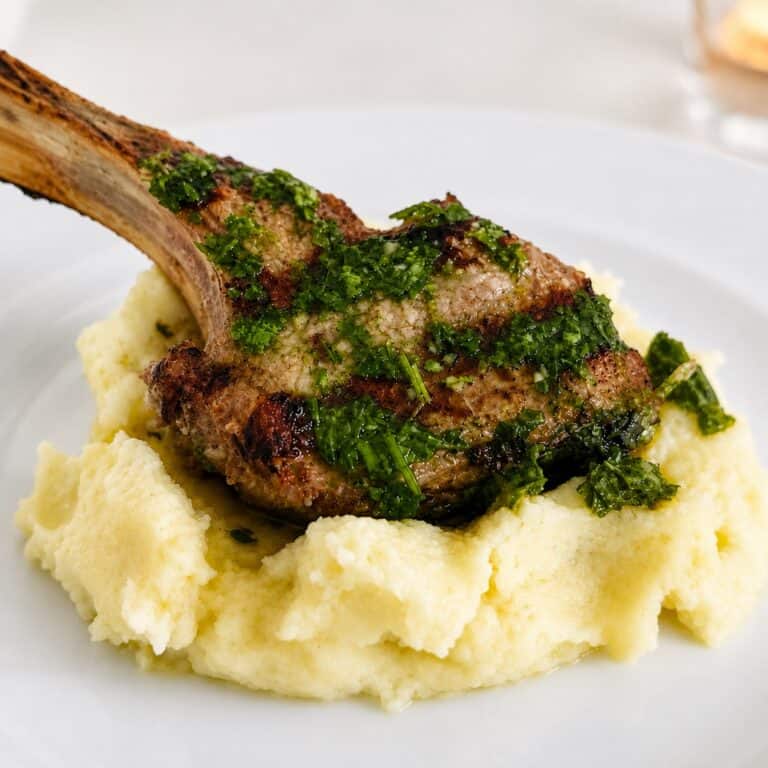 Lamb chop with chimichurri sauce served over creamy mashed potatoes on a white plate.