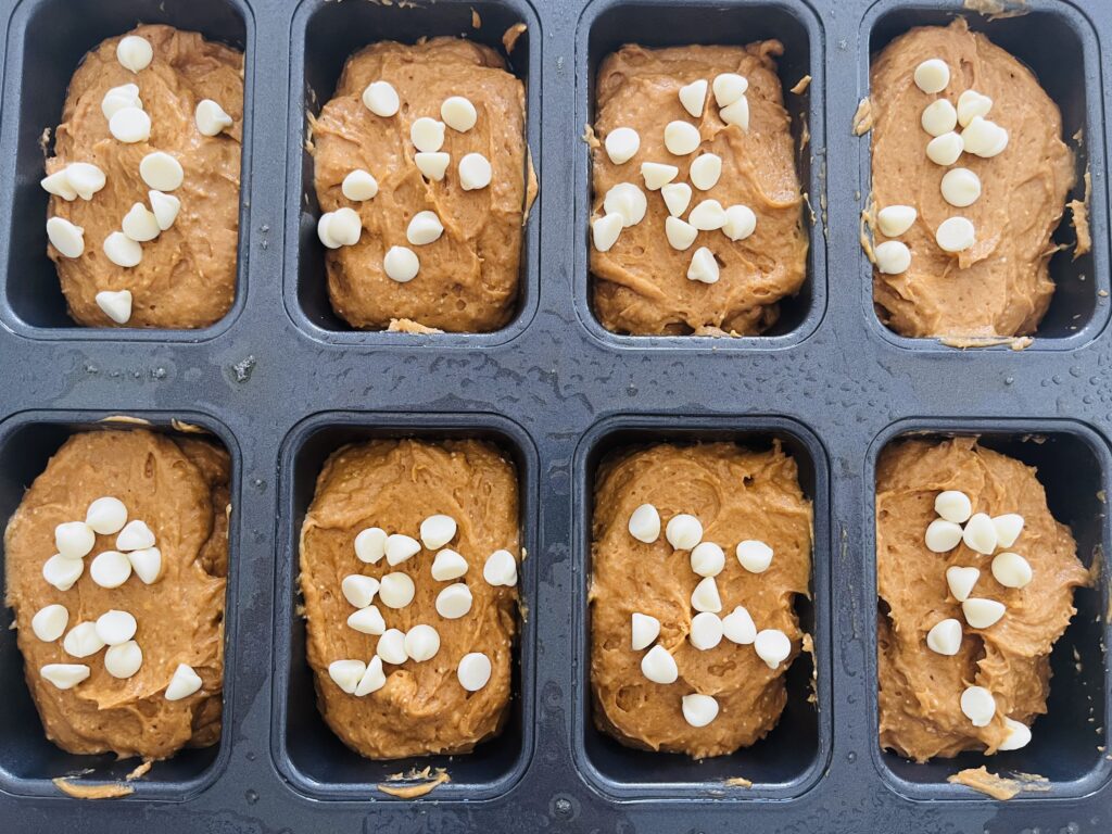 Batter in mini loaf tins with white chocolate chips on top.