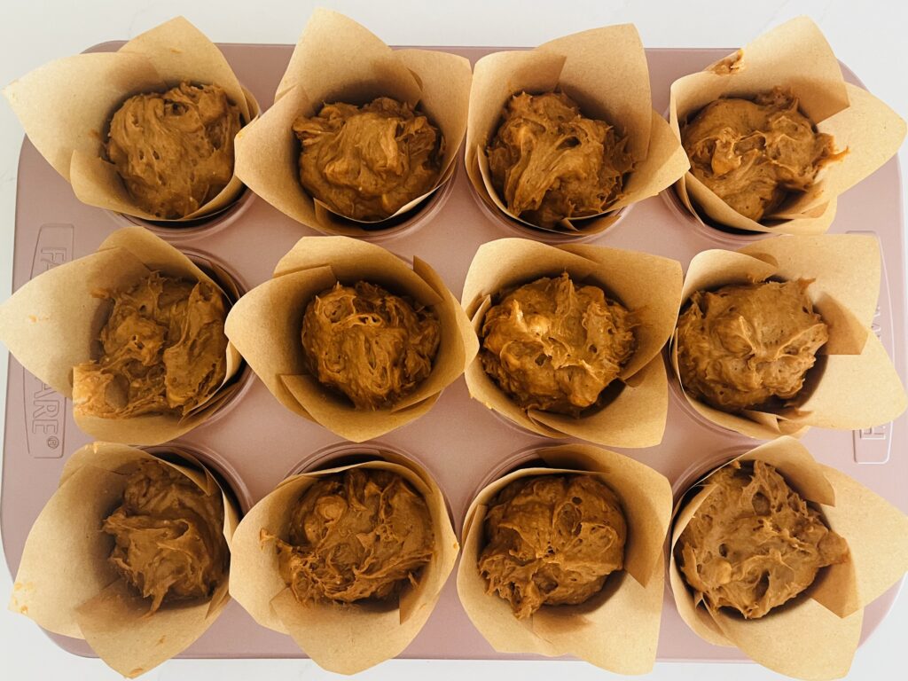 12 large muffin baking cups with batter in muffin cups in a muffing tin on the counter