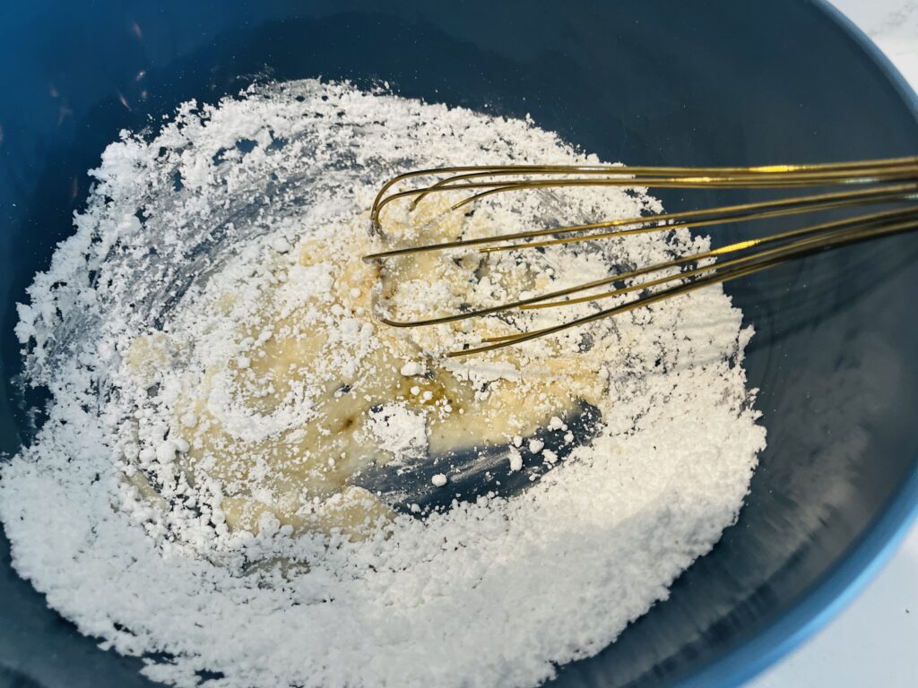 Whisking powdered sugar, vanilla and milk to make icing in a large mixing bowl