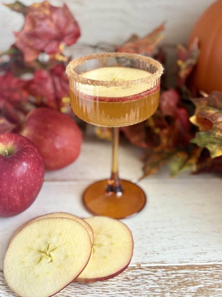 an apple cider spritz in a coupe glass with garnishes of apple slices