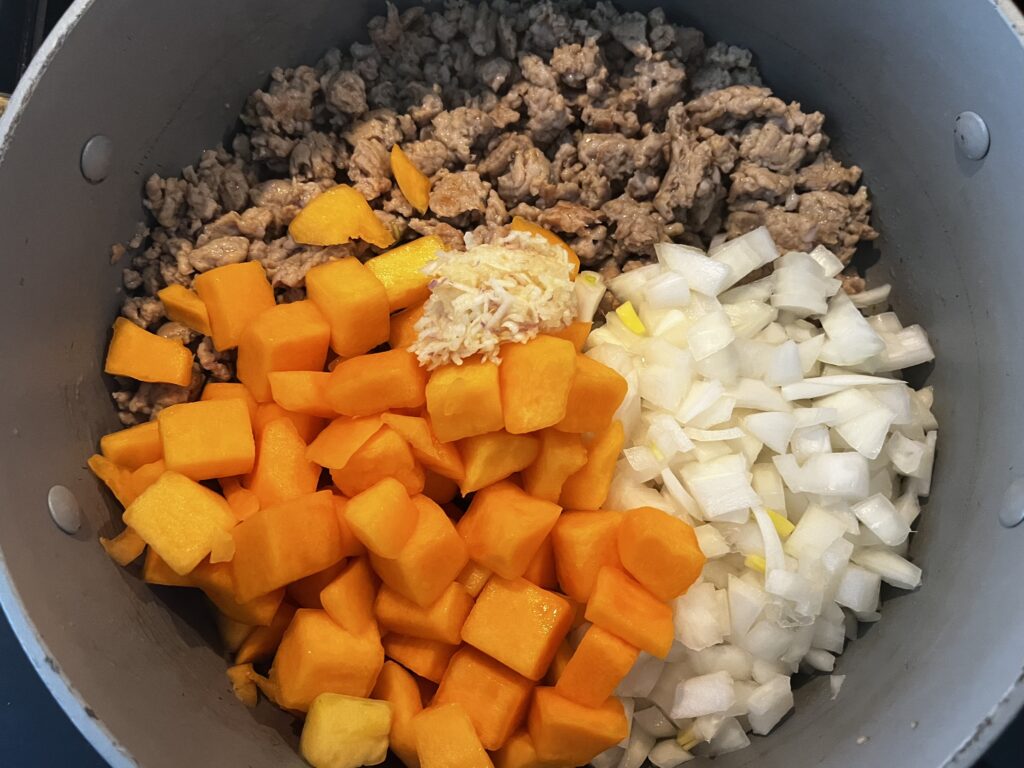 Browned and cooked turkey sausage, onions, garlic and butternut squash in a pot.