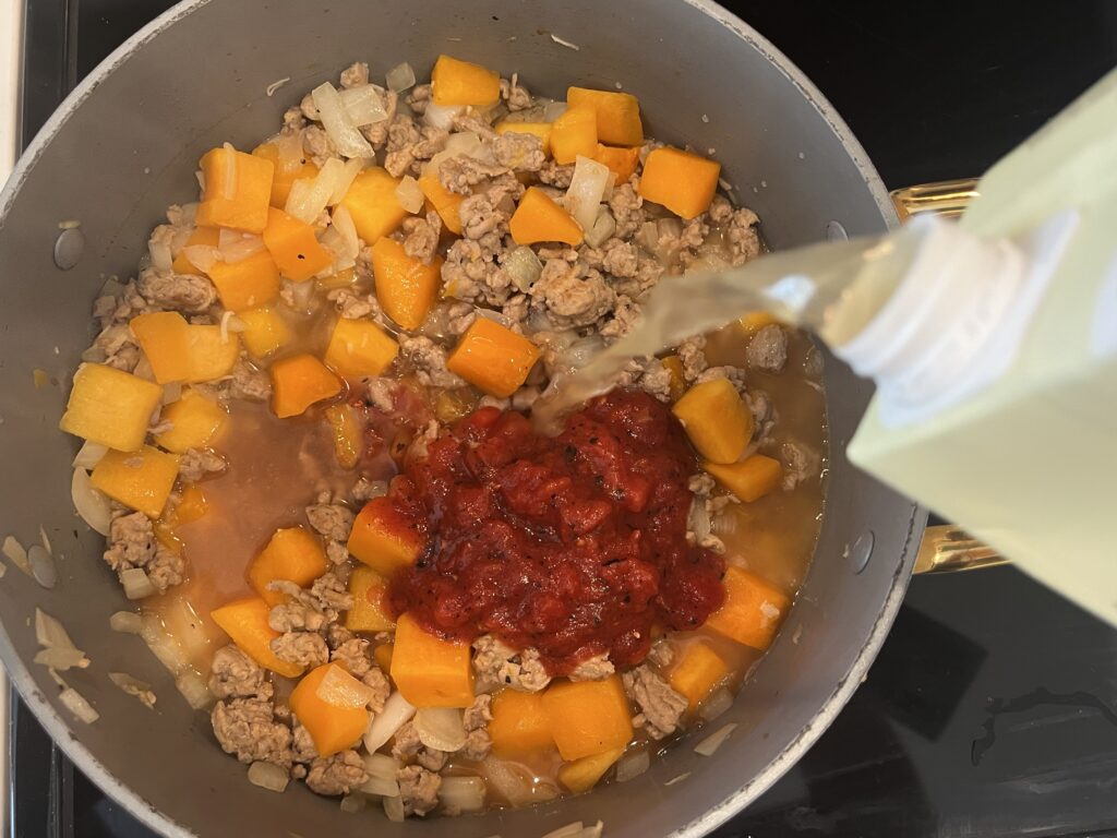 Browned turkey, cooked squash, onions and garlic in a large pot on the stove. Adding chicken broth to pot of ingredients.