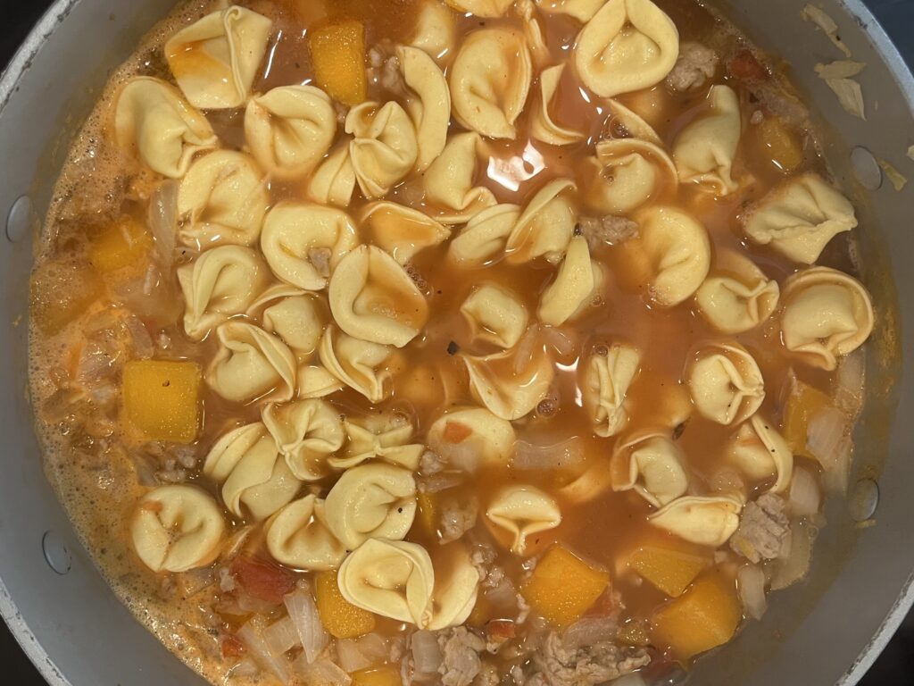 Adding tortellini to the soup pot on the stove