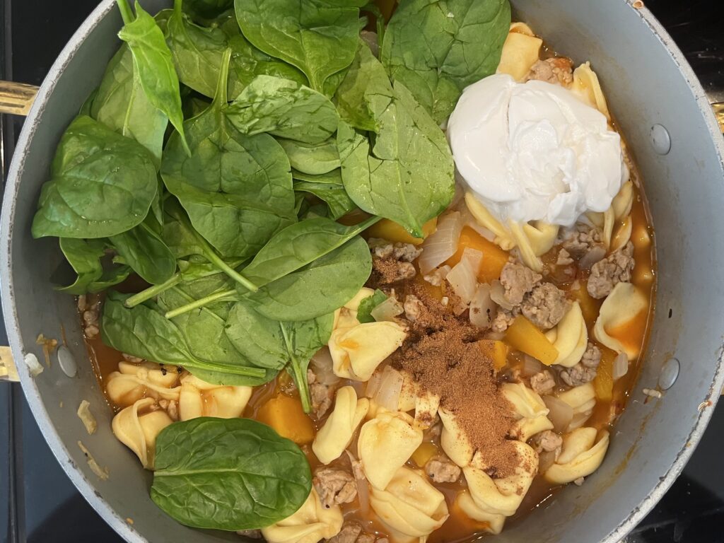 Adding spinach, coconut milk and pumpkin spice to soup pot on the stove