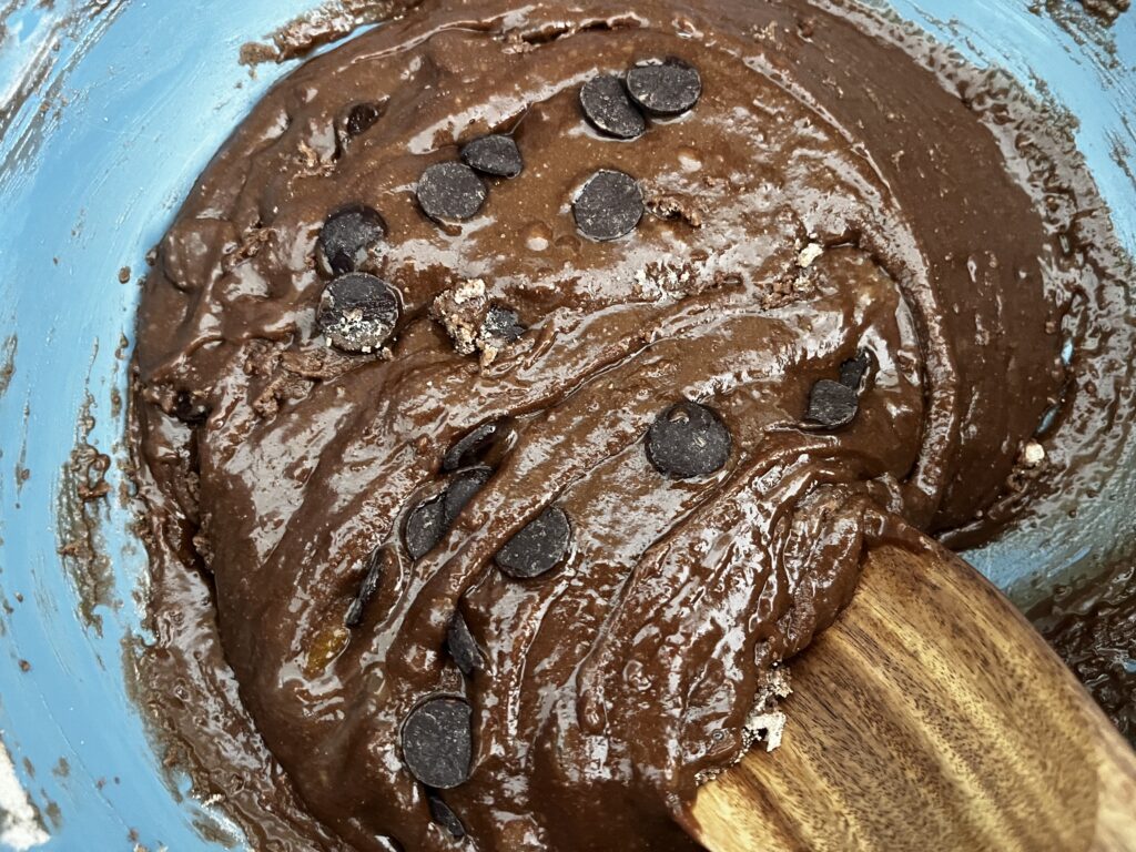 Adding dark chocolate chips to brownie batter in a mixing bowl