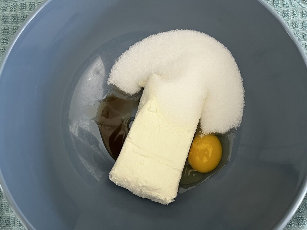 Cream cheese at room temperature, egg, sugar and vanilla extract in a mixing bowl.