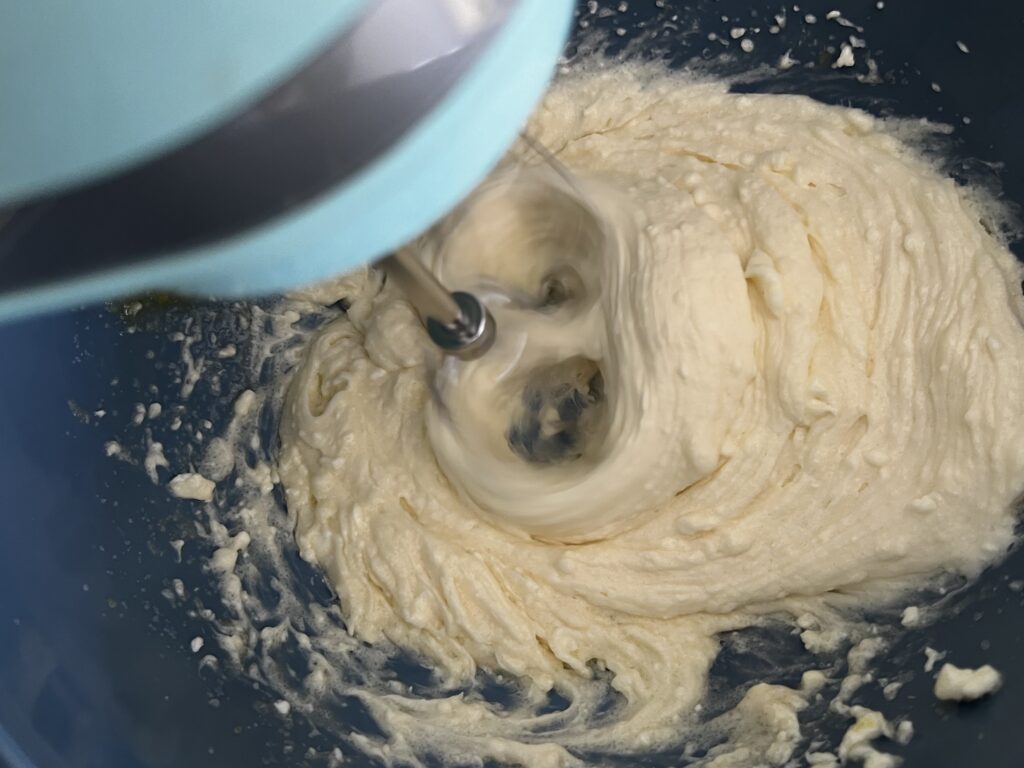 Using an electric hand mixer to combine cream cheese layer ingredients in a mixing bowl.