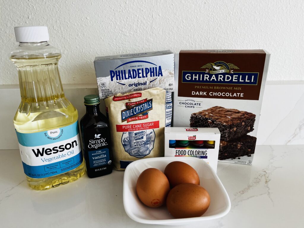 Ghirardelli dark chocolate brownie mix, vegetable oil, eggs,cream cheese-Philadelphia brand used, granulated white sugar, vanilla extract, food coloring box on the counter.