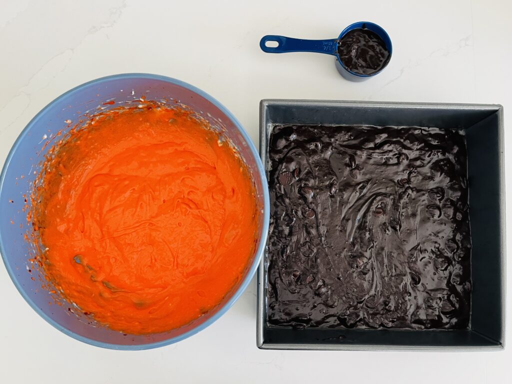 Orange cream cheese layer in a bowl beside brownie batter in a 9x9 baking pan on the counter