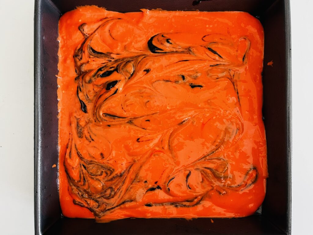 Swirls of brownie batter in the orange cream cheese top layer in a 9x9 baking pan