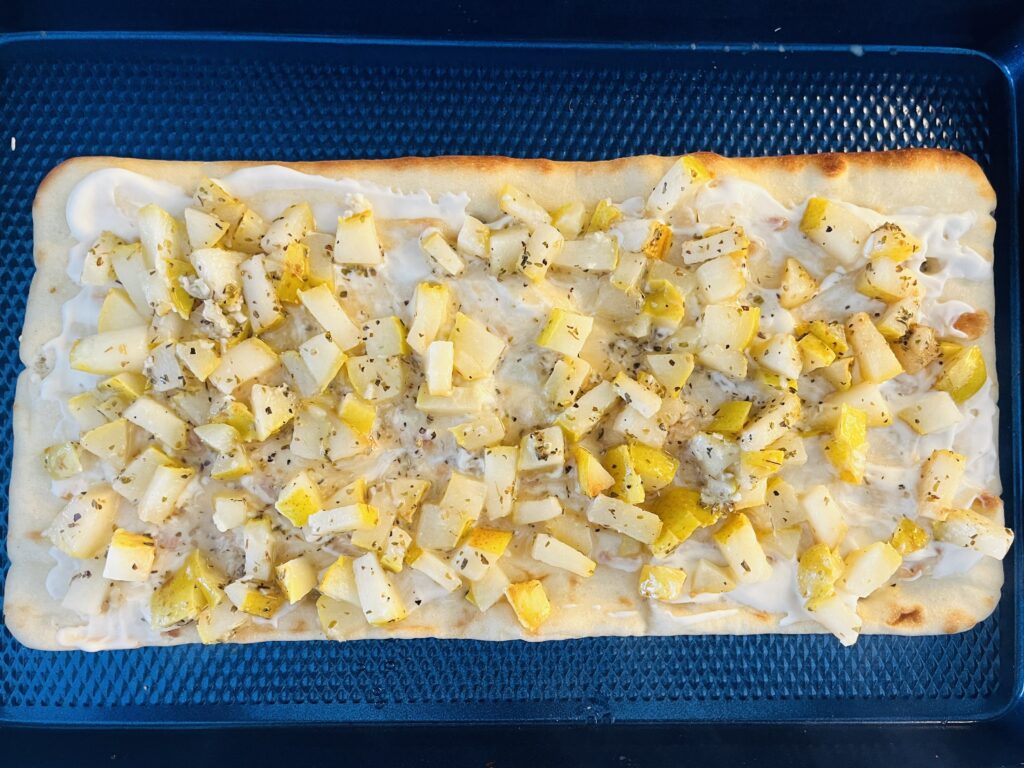 Flatbread topped with Alfredo sauce and cooked pears on a baking sheet